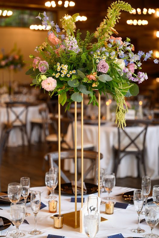 Tall floral centerpiece with candles under string lights at a mountain lodge reception