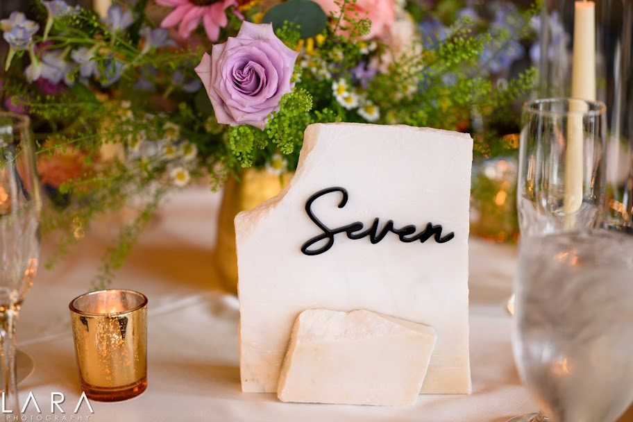 Hand-lettered table seven card among wildflowers at a mountain wedding reception