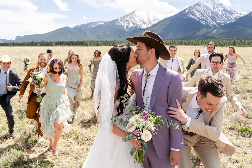 Couple and their wedding party walking through a mountain meadow, laughing